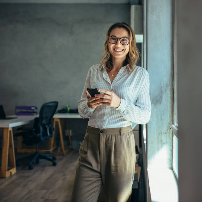 Smart looking woman in office with smartphone.