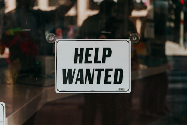 Oznam na dverách s textom help wanted. Pracovná ponuka